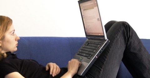 photo of woman sitting on blue sofa with laptop