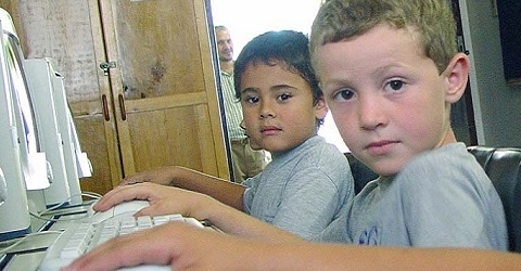 photo of three children sitting in front of computers