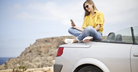 woman using mobile phone sat on a car at the beach