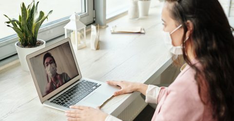 a woman wearing a surgical face mask using a laptop to have a video call with a man wearing a surgical face mask 